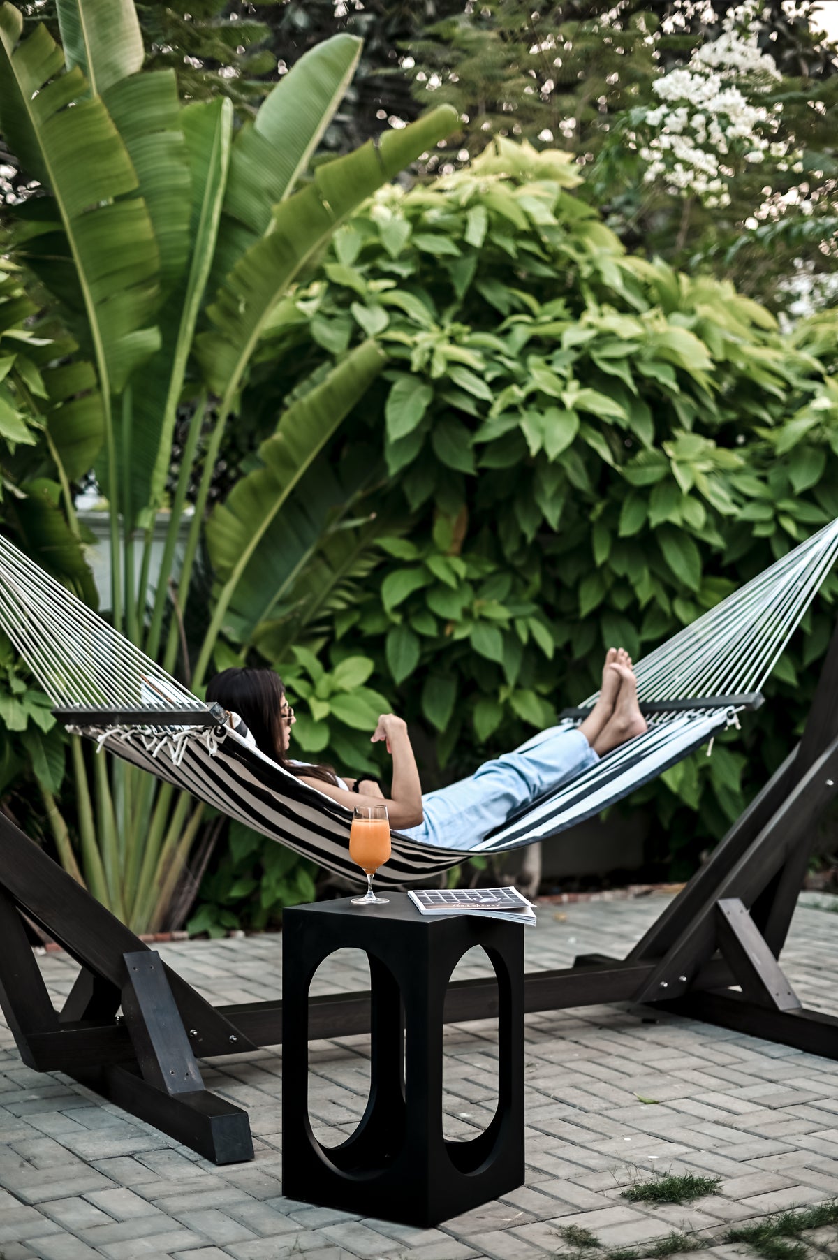 Standalone Wooden Hammock - Sculptural black wooden frame with a striped woven textile in a lush garden setting by Ali Khan Studio Karachi Pakistan