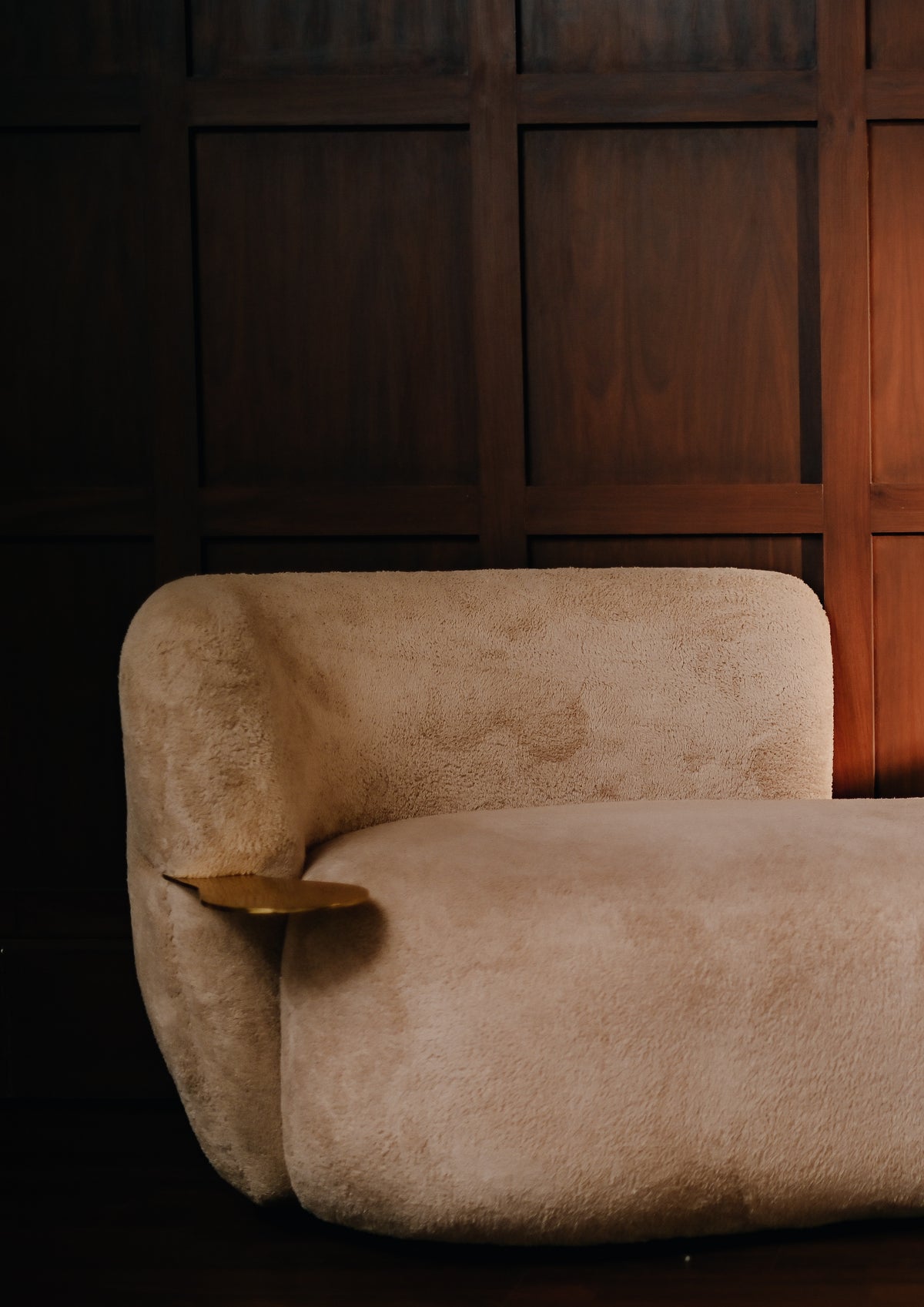 Close-up of the Cloud Sofa featuring high-tactility beige upholstery and a hand-cast brass integrated side table against a dark wood-paneled wall.
